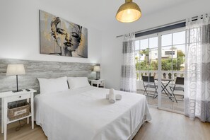 Habitación de hotel con cama, mesita de noche, lámpara, un cuadro en la pared y vistas al exterior.