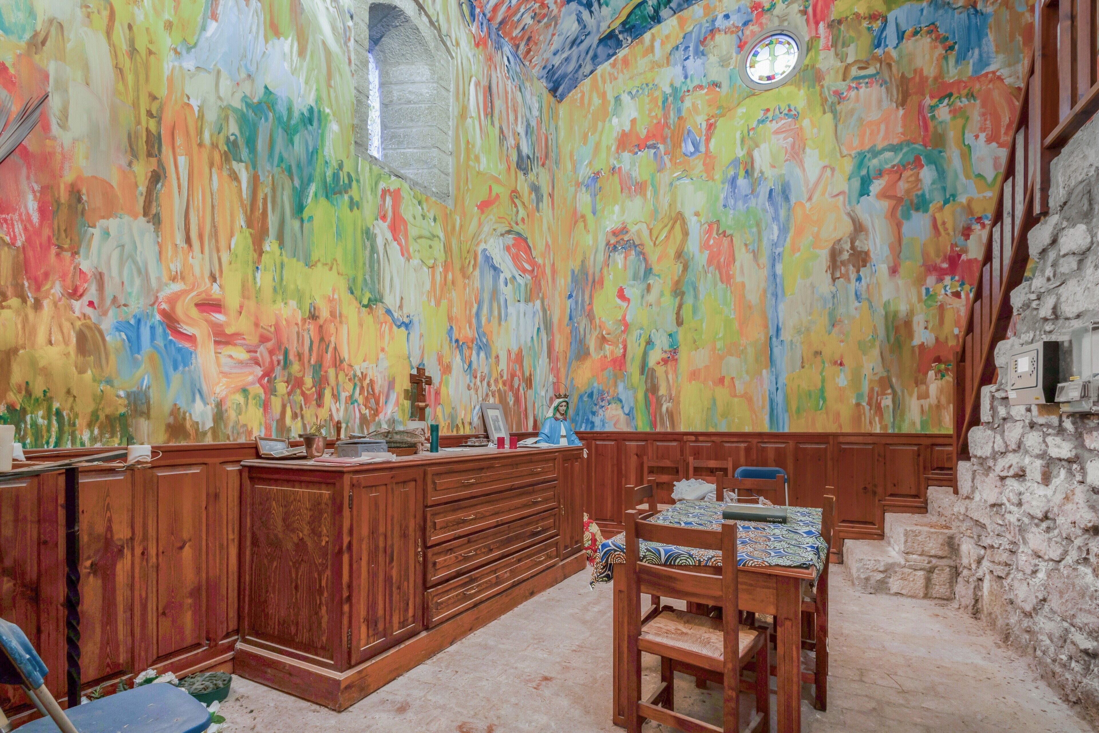 Una stanza con una scrivania in legno, sedie, un muro in pietra e un murale astratto dai colori vivaci.