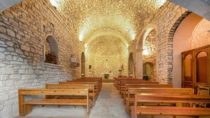 Interior de iglesia con paredes de piedra, bancos de madera y un pasillo central que conduce a un altar.