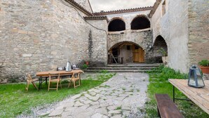 Un patio con paredes de piedra, una mesa de madera, sillas y un banco.