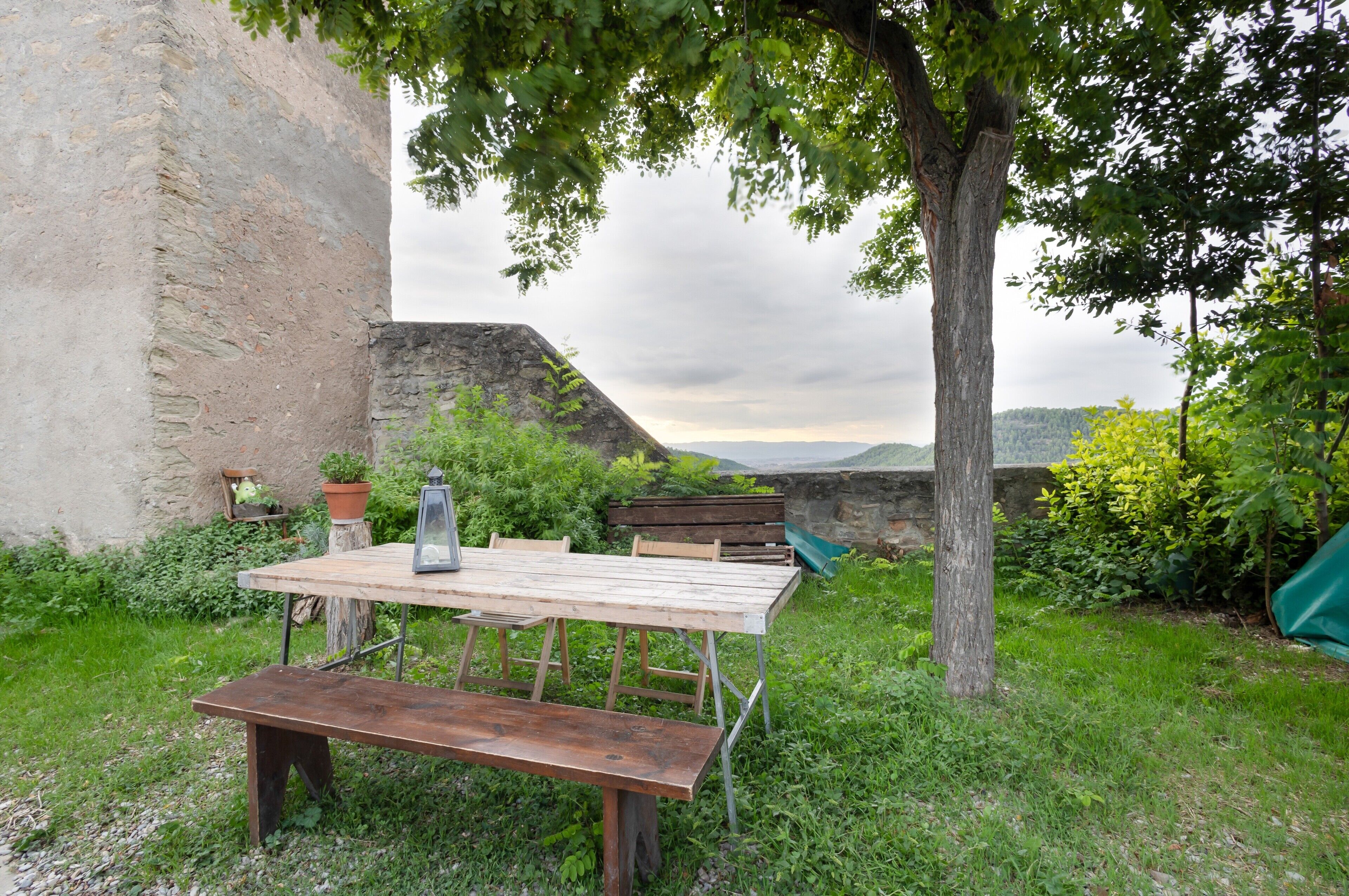 An outdoor table and bench set in a garden with a stone wall and greenery.