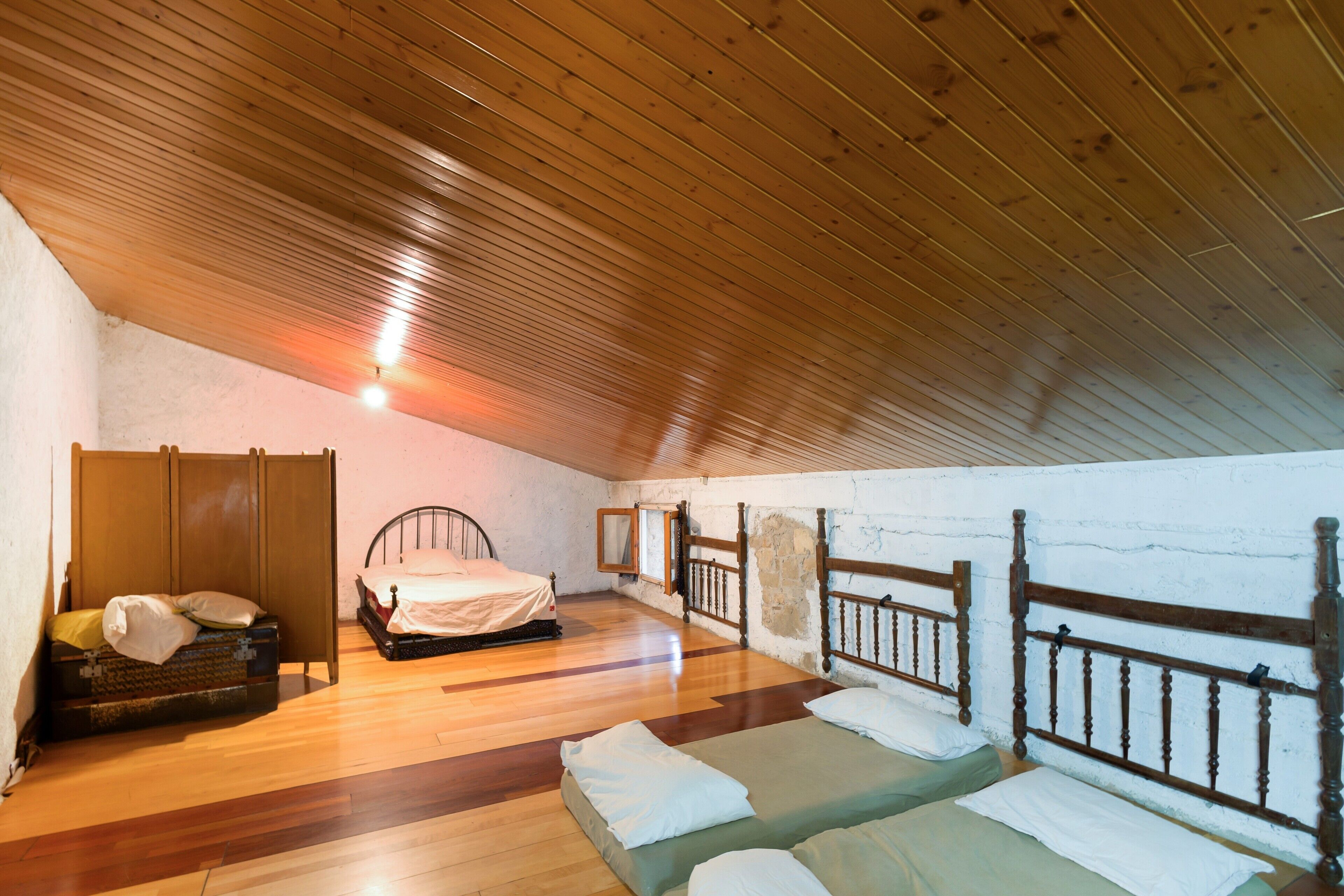 A room with a sloped ceiling, wooden flooring, two beds with wooden headboards, a wardrobe, and a mirror on the wall.