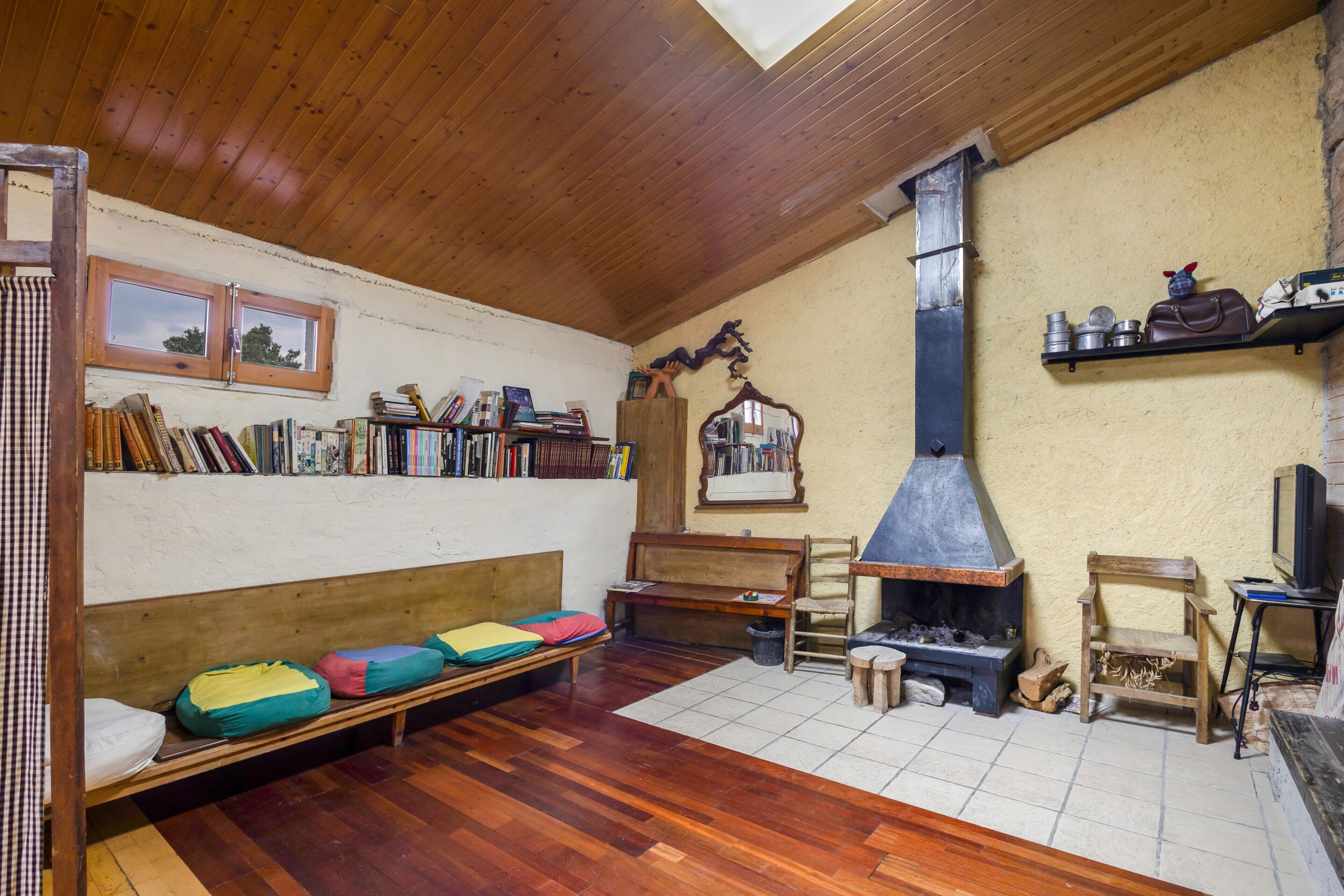 A cozy room with a wooden ceiling, a fireplace, a bookshelf, a bench, and a television.