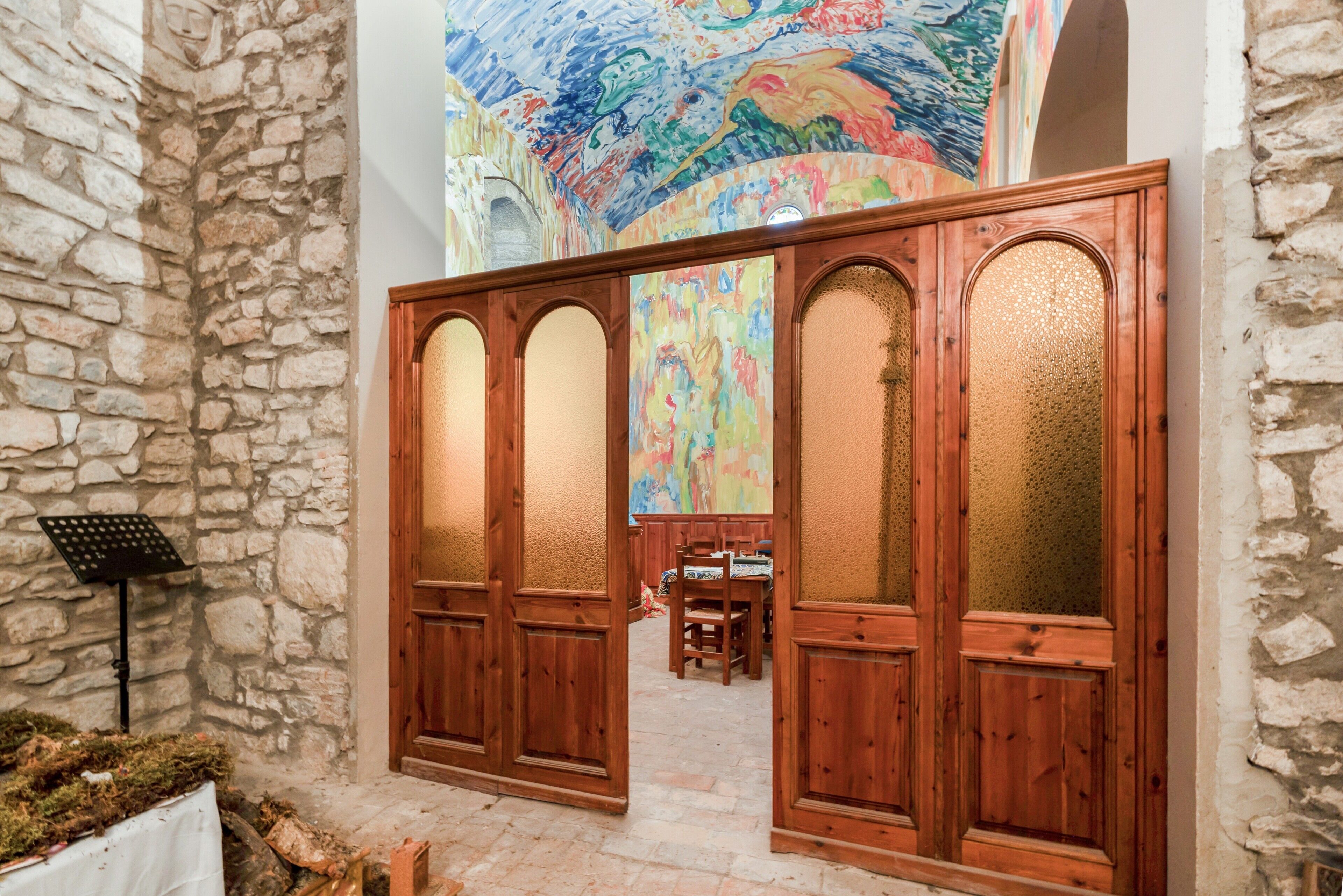 A stone wall, wooden doors with glass panels, a colorful mural, and a table with a music stand.