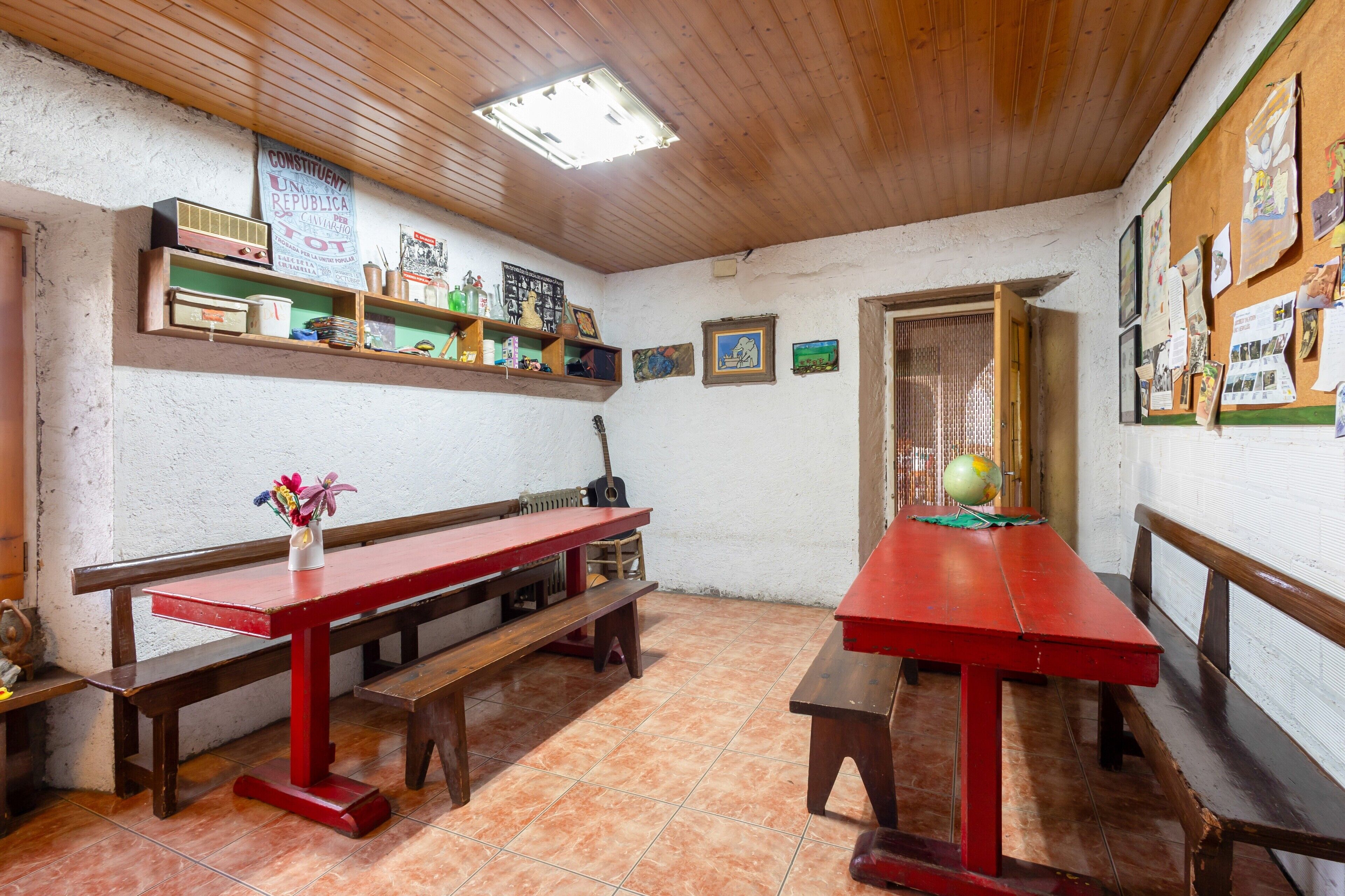 Une pièce rustique avec des bancs en bois, une table rouge et des étagères remplies de divers objets.