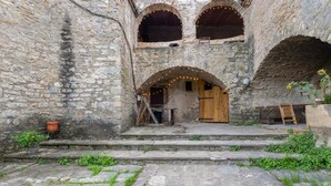 Un edificio de piedra con arcos, una puerta de madera y un pequeño espacio exterior con escalones que conducen a la entrada.