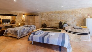 Un dormitorio con dos camas, una pared de piedra, una piscina pequeña y un banco de piedra.