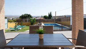 Un patio con mesa y sillas, una planta pequeña en maceta, una piscina y vistas del entorno.