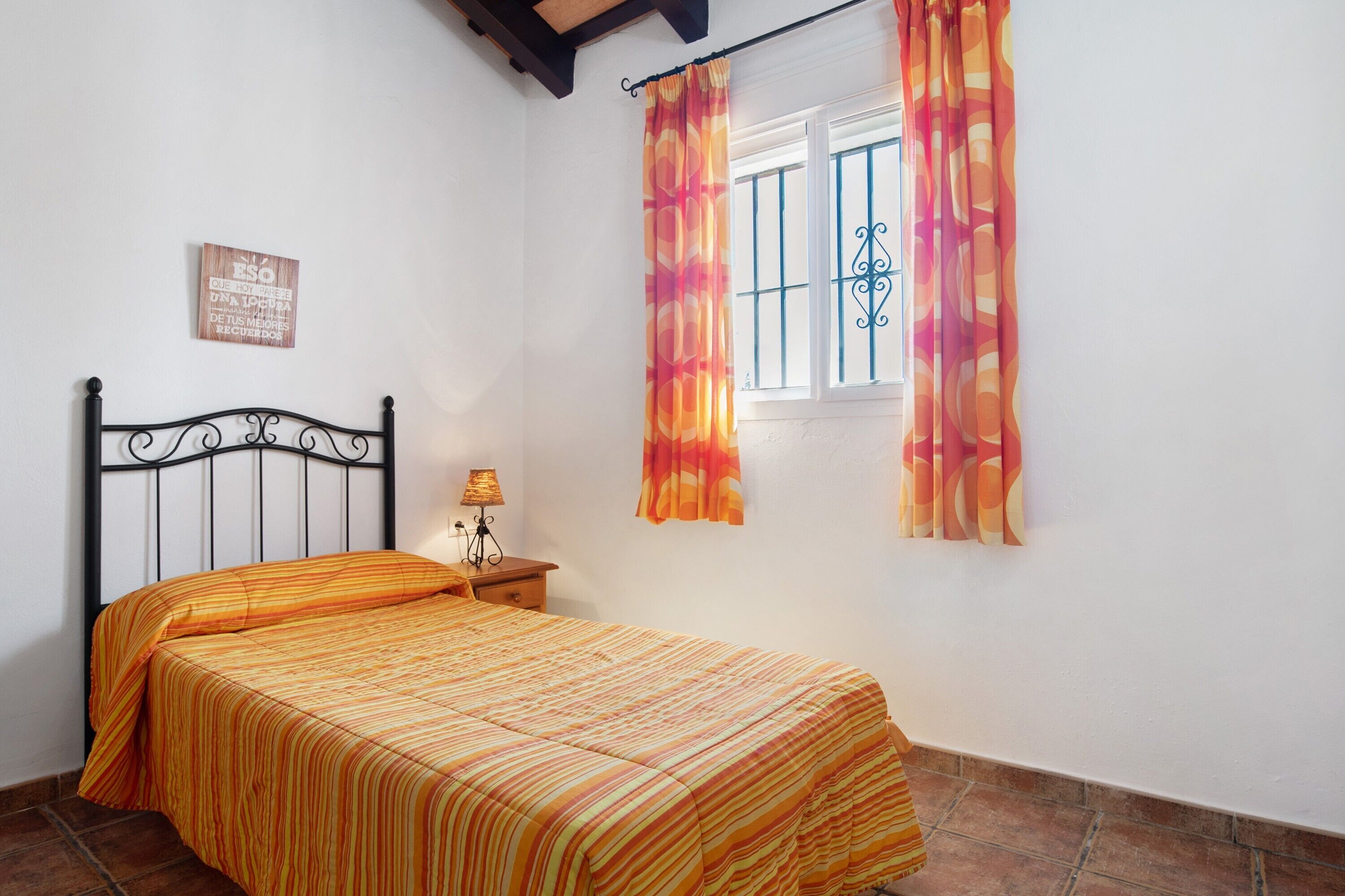 Une chambre à coucher comprenant un lit, une table de chevet, une lampe, une fenêtre avec des rideaux et un élément décoratif mural.