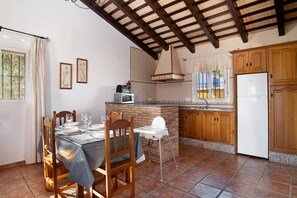 A kitchen with a dining table, chairs, a baby high chair, a refrigerator, wooden cabinets, a microwave, and a window with curtains.