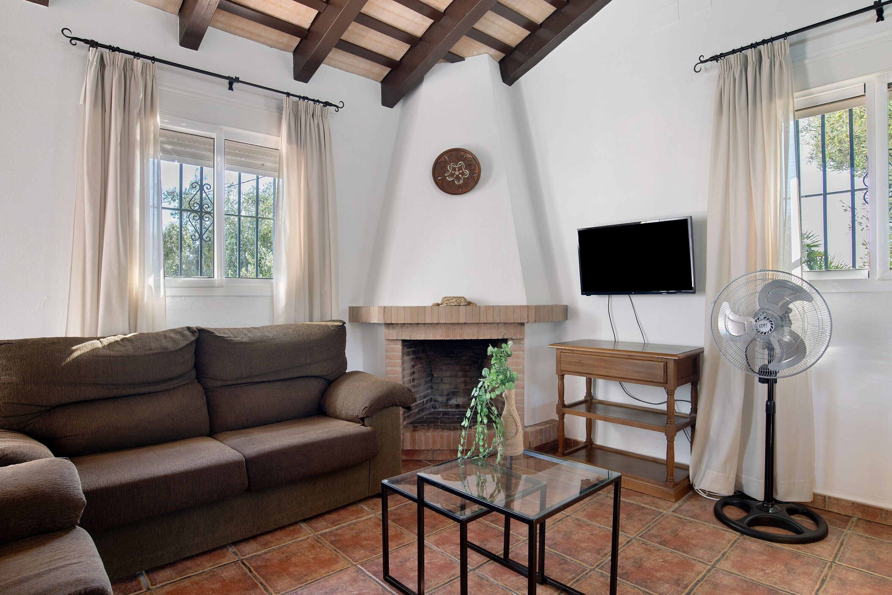 A living room with a sofa, a glass coffee table, a fireplace, a TV, and a fan.