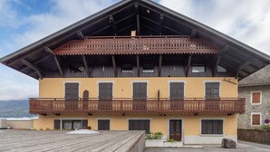 Un immeuble à plusieurs étages doté d’un balcon, de poutres en bois et surplombant un paysage montagneux.