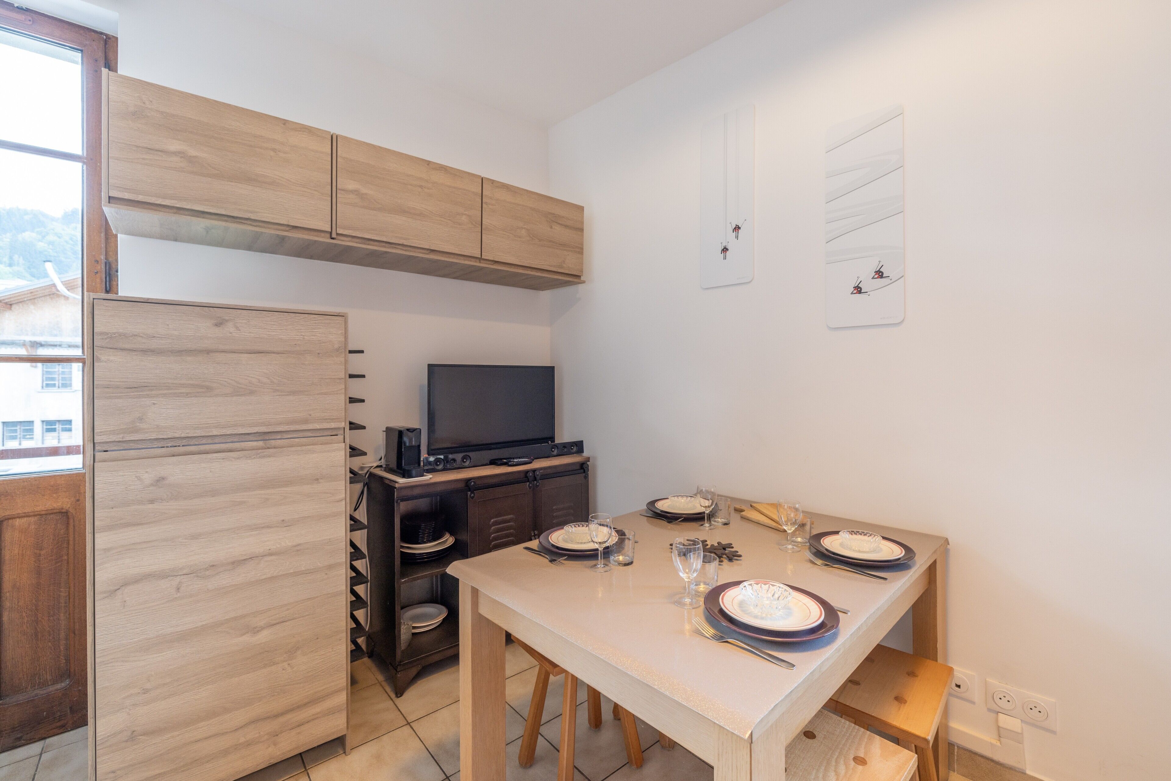 Een kleine keuken met houten kastjes, een eettafel voor vier personen en een televisie op een standaard.