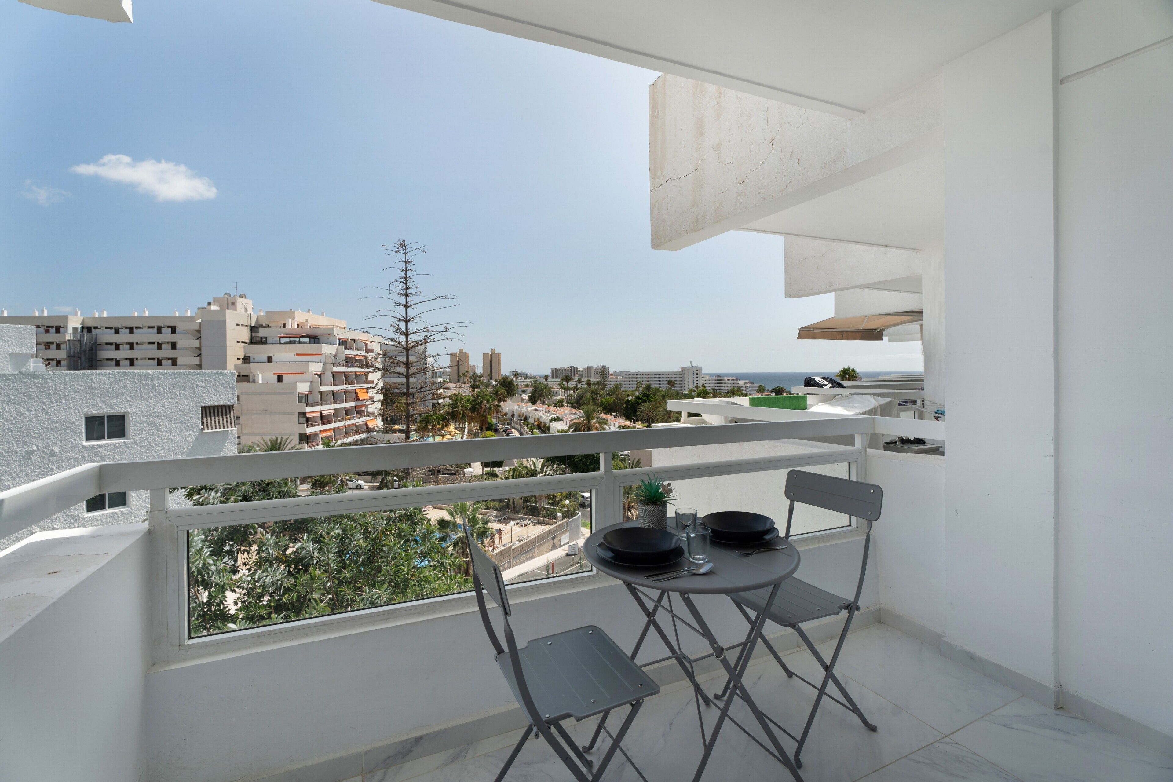 A balcony with a table set for two, a chair, and a view of the cityscape.