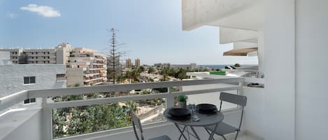 A balcony with a table set for two, a chair, and a view of the cityscape.