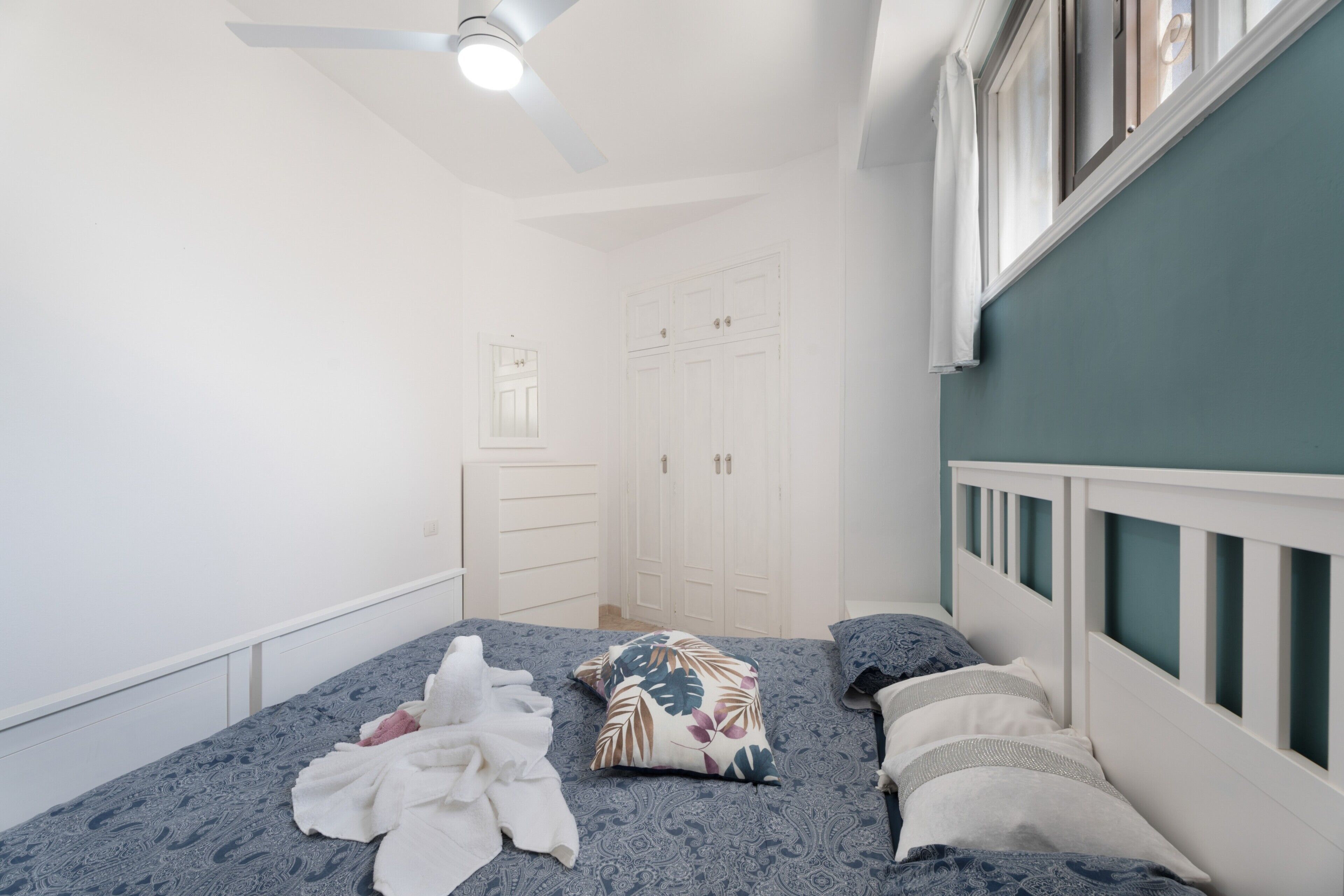 A bedroom with a bed, white wardrobe, and a ceiling fan.