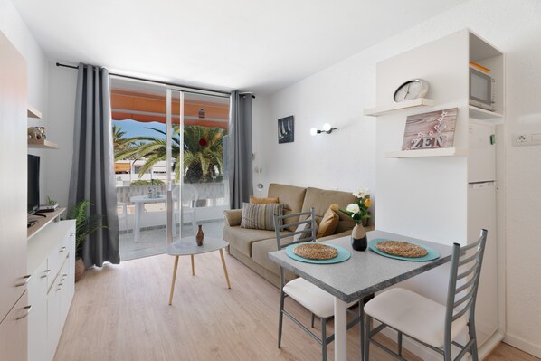 A modern living space with a dining area, a sofa, a TV, and a balcony with plants.