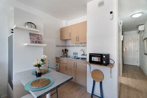 A compact kitchen with wooden cabinets, a microwave, and a small dining area with a table and chairs.