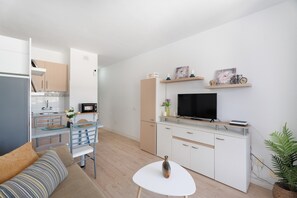 A compact living space with a kitchenette, a dining area, a sofa, a TV, and a small table.