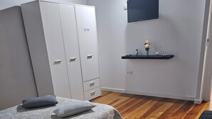 A bedroom with a bed, a wardrobe, a TV, a shelf with items, and a chair.
