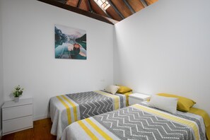 A bedroom with two beds, a nightstand, a small table, and a painting on the wall.