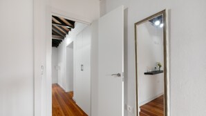 A hallway with wooden flooring, white walls, and a large mirror on one side.