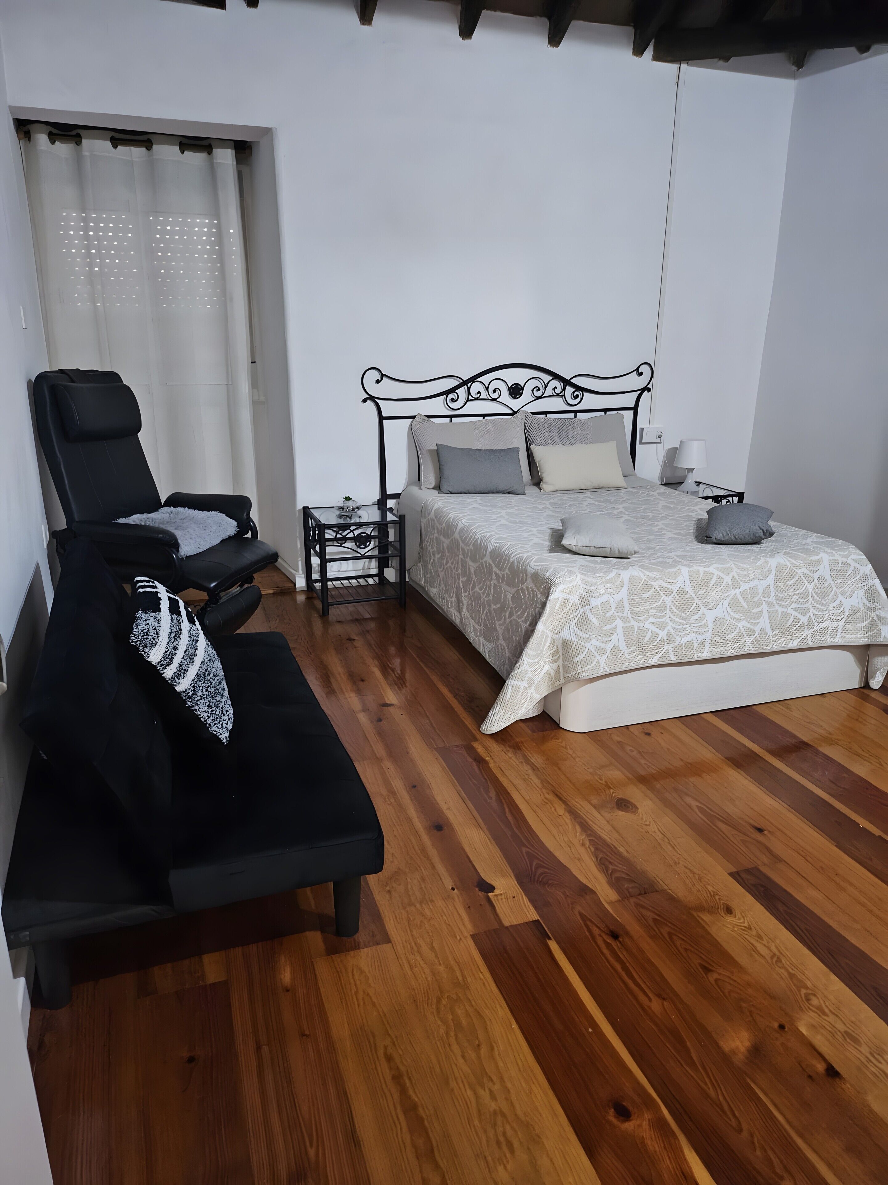 Une chambre à coucher avec un lit, une chaise, une petite table et une fenêtre avec des rideaux.