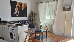 A living room with a sofa, a small table, a washing machine, and a ceiling with exposed beams.