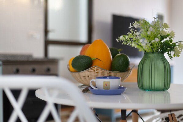 A dining table with a basket of fruits, a cup, and a green vase with flowers.