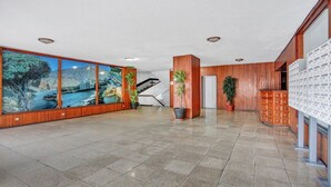 Een ruime lobby met betegelde vloer, houten lambrisering, een trap, potplanten en een groot wandmontage scherm.