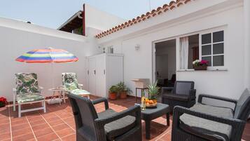 An outdoor patio with wicker furniture, a colorful umbrella, and potted plants.