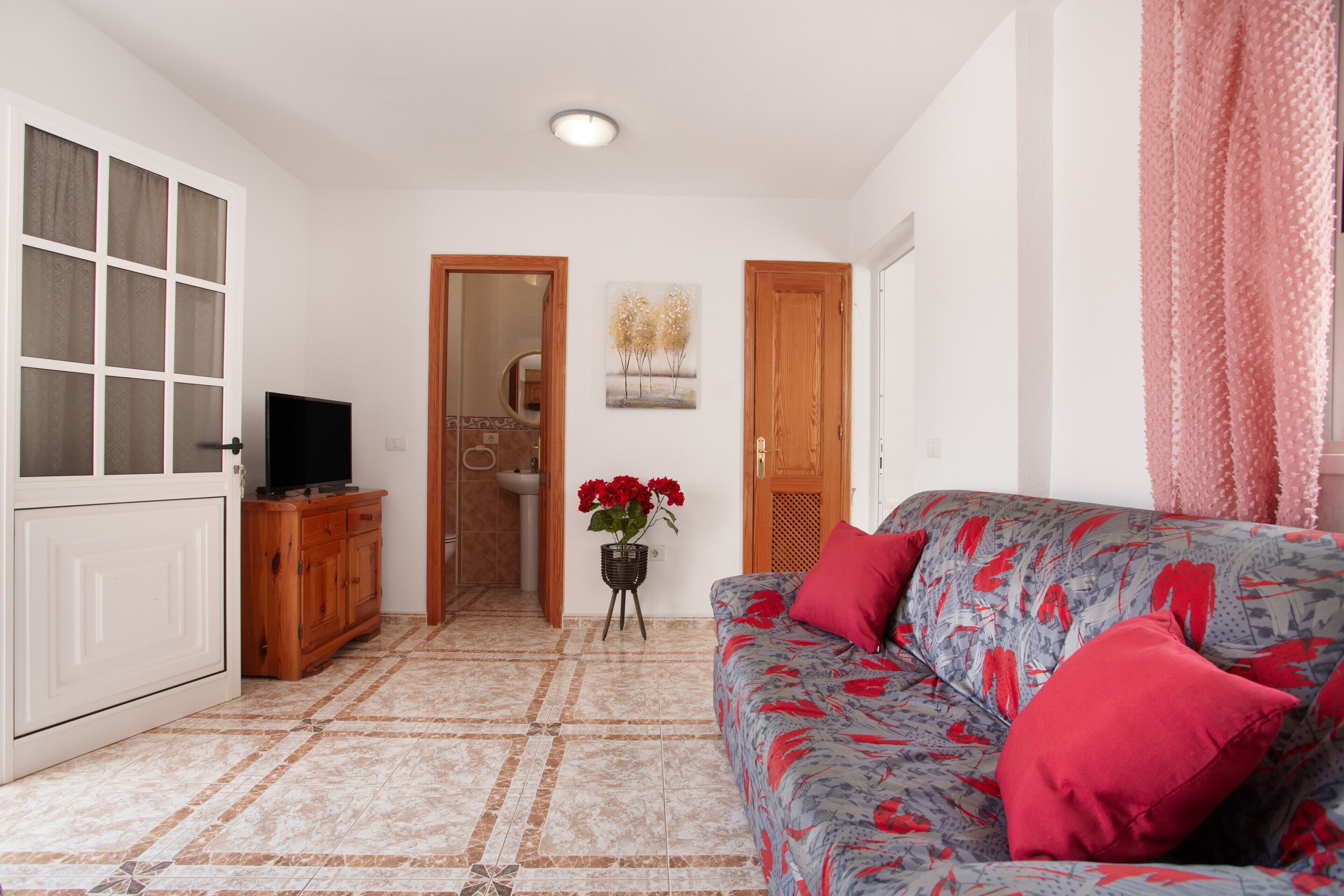 Una sala de estar con sofá, televisor, aparador y una puerta que da a un baño.