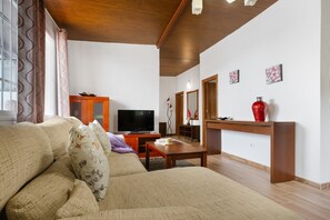 Un salon avec un canapé, un téléviseur, un meuble en bois et un vase rouge posé sur une console.