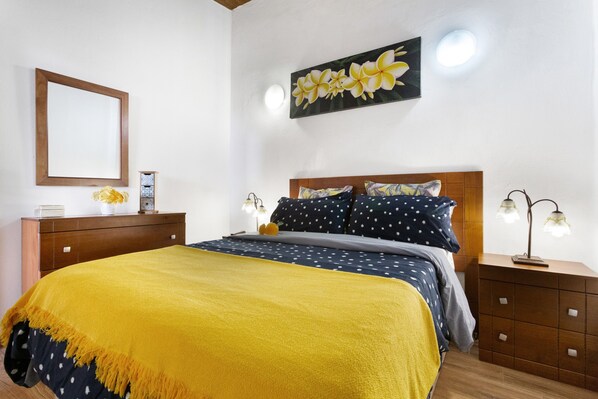 Une chambre à coucher comprenant un lit, une table de chevet, une commode, un miroir et une œuvre d’art accrochée au mur.