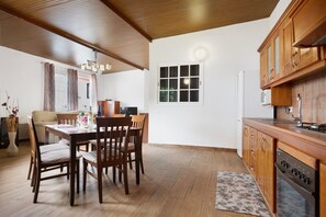 Une cuisine avec des meubles de rangement en bois, une table à manger avec des chaises et une fenêtre avec des rideaux.