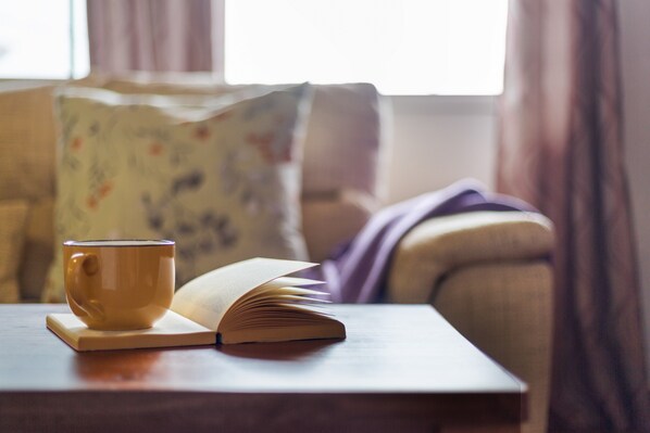 A book and a cup on a table in a room with a couch and a window.