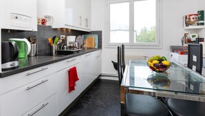 A modern kitchen with white cabinets, a black countertop, and a glass dining table with a fruit bowl. - La Ville Allis by Interhome (Saint Malo)