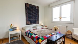 A bedroom with a large bed, a bedside table with a lamp, a window with a star decoration, and a radiator. - La Ville Allis by Interhome (Saint Malo)