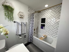 Ein modernes Badezimmer mit Fischgrätmuster, einer Dusche mit Glastür, einer Badewanne und einem WC.