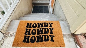 A set of concrete steps leading to a door with a doormat that reads "HOWDY HOWDY HOWDY". - Westerhaven | Western-Themed Garden Suite • Pet Friendly • 2 Queen Beds • Near I-84 • Nampa (Nampa)