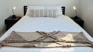 A neatly made bed with a white comforter and striped pillows, a framed animal illustration on the wall, and two bedside lamps on wooden nightstands. - Westerhaven | Western-Themed Garden Suite • Pet Friendly • 2 Queen Beds • Near I-84 • Nampa (Nampa)