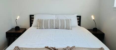 A neatly made bed with a white comforter and striped pillows, a framed animal illustration on the wall, and two bedside lamps on wooden nightstands.