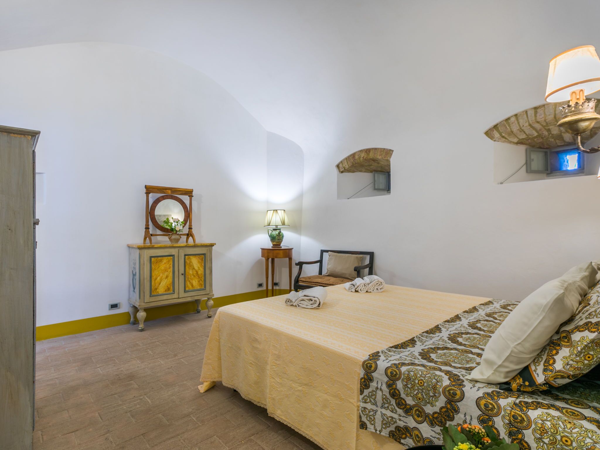 Ein Schlafzimmer mit Bett, Nachttisch, Kommode, Spiegel und einer Wandlampe.