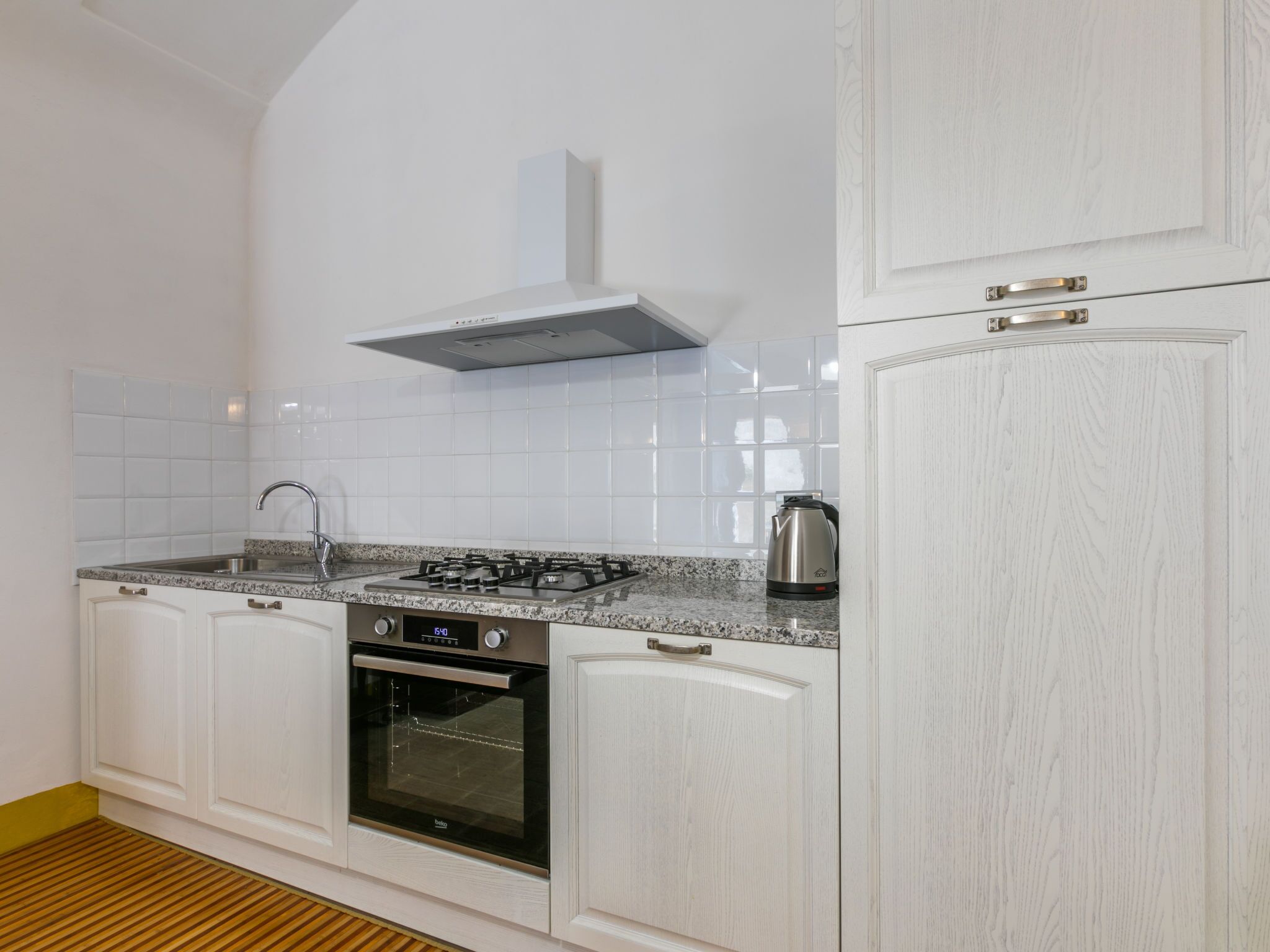 A modern kitchen with white cabinetry, a stainless steel stove, and a built-in oven.
