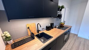 Cozinha moderna com armários escuros, bancada de madeira, pia, cafeteira e uma fruteira.