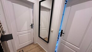Um corredor com portas brancas, um espelho grande e uma estante de metal.