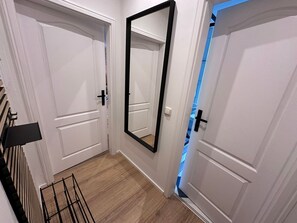 A hallway with white doors, a large mirror, and a metal rack.