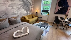 Quarto com cama, sofá, tapete de zebra, escrivaninha e cadeiras, e janela com vista para árvores.