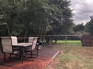 An outdoor deck with a table and chairs, surrounded by a wooden fence and trees. - Charming 2-bedroom cottage located on a beautiful property. AC, Wifi, & laundry (Durham)