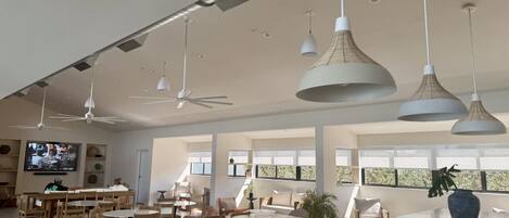 A spacious living area with a large dining table, multiple seating arrangements, ceiling fans, and pendant lighting.
